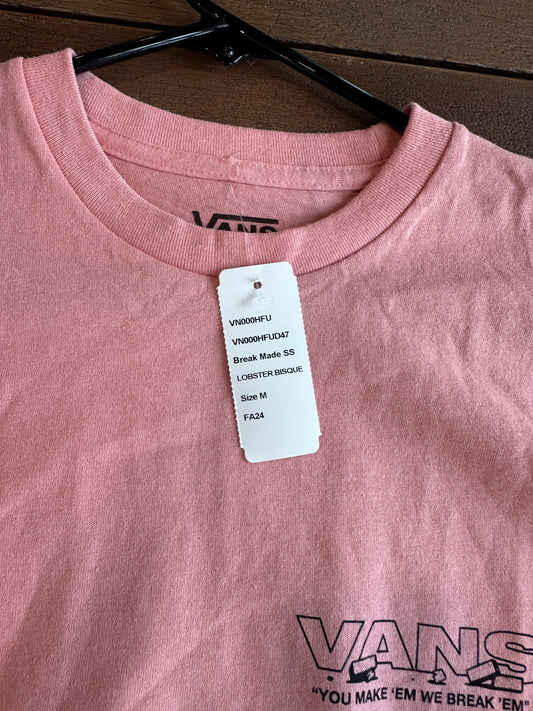 Pink t-shirt with a tag and Vans logo on a brown surface